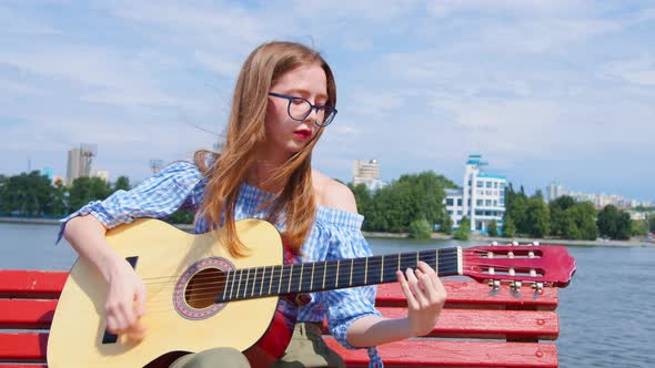 A Woman Is Playing the Acoustic Guitar Outdoors alt