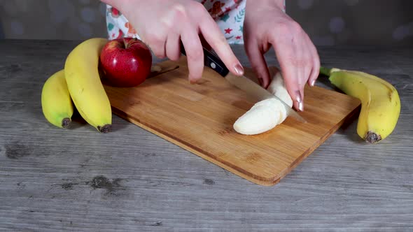 A woman in a kitchen cutting up a banana on a chopping board alt