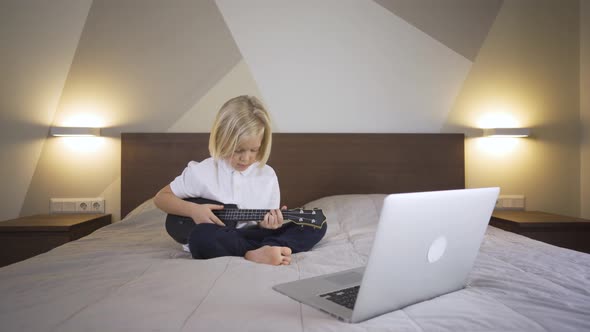 Distance Learning Online Education. A Pre School Boy Learning To Play the Ukulele on Laptop at Home.