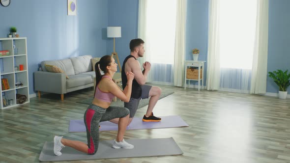 Active Couple Is Doing Forward Lunges at Home alt