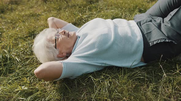 Cool Grandma Lying on the Grass with Hands Under Her Head. Resting in Nature alt