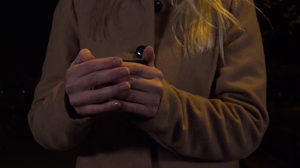 A Woman Drinks a Hot Drink From a Mug in an Urban Area at Night - Closeup alt