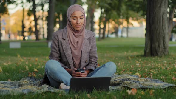 Islamic Muslim Girl Student Online Teacher Business Woman in Hijab Sitting in Park on Green Grass alt