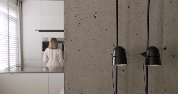 A Woman Makes a Coffee in a Minimalist Interior with Focus on the Lamp alt