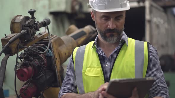 Male engineer foreman controlling robotic arm with digital tablet