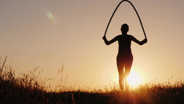Training in the Fresh Air - a Silhouette of a Woman Jumping Over a Rope at Sunset alt