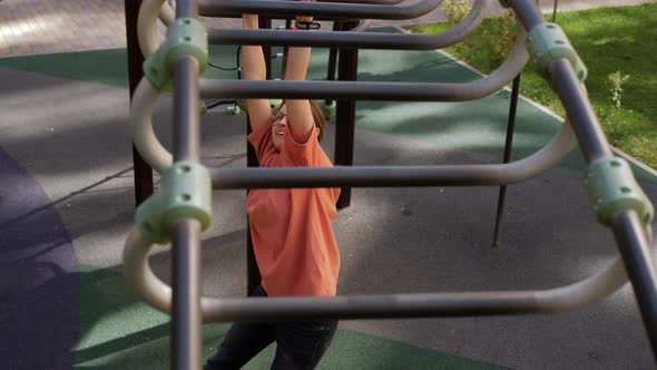 A Teenage Girl on Monkey Bars Crawls on a Children's Playground