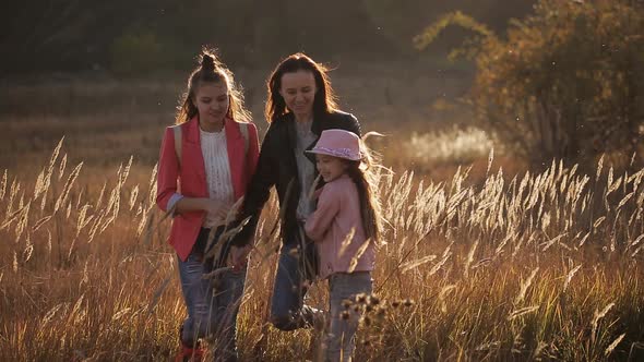 A Happy Mother and Her Two Daughters are Walking Around the Field in the Steppe at Sunset
