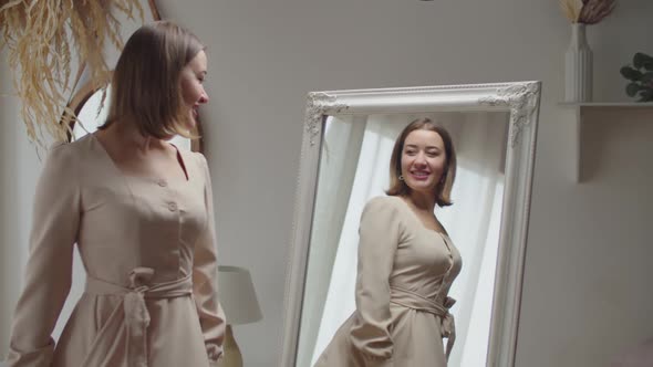 Joyful Lovely Adult Woman in New Dress Admiring Her Appearance in Mirror at Home alt