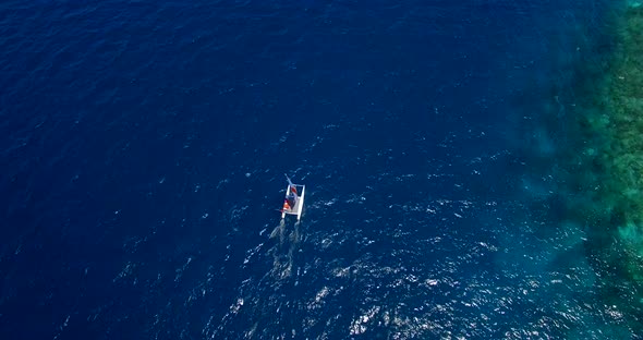 Aerial drone view of a man and woman sailing on a boat to a tropical island. alt