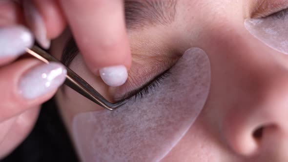 A Young Woman Undergoes an Extension Procedure the Master Removes Old Eyelashes with Tweezers in a alt