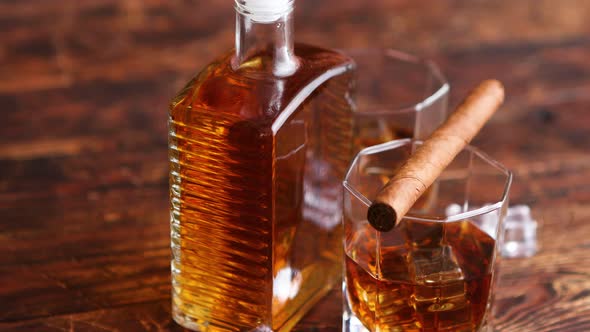 Bottle of Whiskey with Two Glasses and Cuban Cigar Placed on Rustic Wooden Table