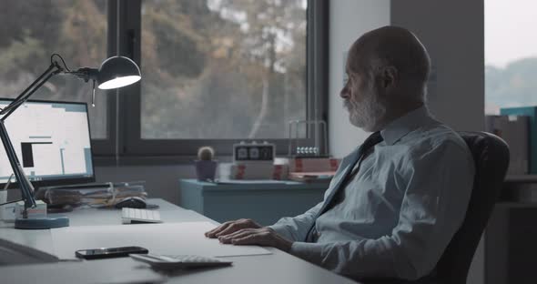 Bored businessman sitting at desk and doing nothing, he is looking out the window