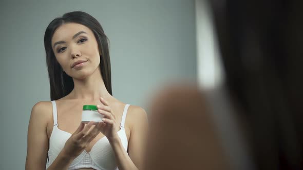 Beautiful Asian Girl Putting Cream on Face, Standing in Front of Mirror, Beauty alt