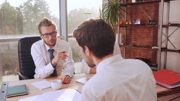 Male Job Applicant in White Shirt Speaking with Caucasian Boss in Glasses Sitting at Table with alt