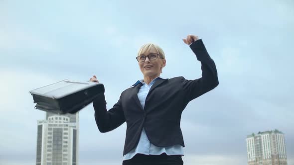 Happy Woman in Office Suit Holding Bag and Raising Hands in Victory Gesture