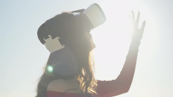 Close-up of Happy Young Brunette Woman in VR-glasses Standing in Sunrays Outdoors. Portrait of alt