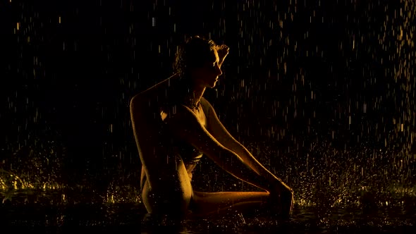 Exercise the Leg Behind the Head. Young Woman Practices Yoga Asanas in a Dark Studio in the Rain alt