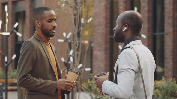 Two Black Businessmen Holding Coffee and Talking on Street alt