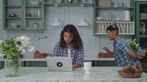 Young Adult African American Man in Birthday Hat Making Surprise for His Wife with Birthday Gift