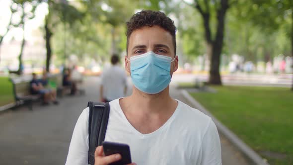 A Young Handsome Man Stands in the Park in the Alley Wearing a Protective Mask During the alt
