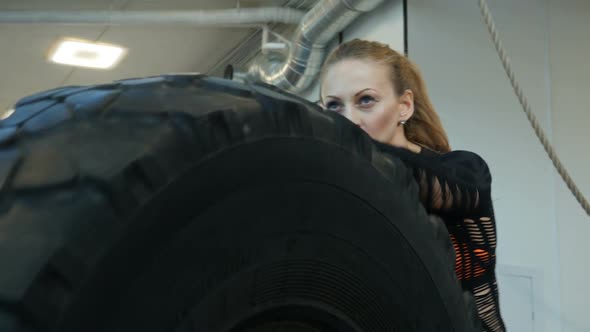 Caucasian athlete rolls big tires in the gym. Young woman exercising crossfit
