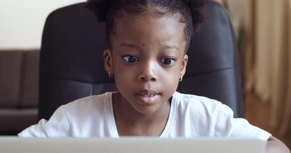 Funny Little African Girl Looking at Web Camera or Screen of Laptop Sitting at Home, Cute Kid alt
