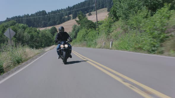 Tracking shot of man riding motorcycle on country road.  Fully released for commercial use.