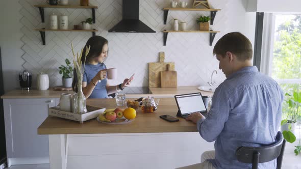 Woman with Phone and Man with Laptop Sit at Table in Kitchen