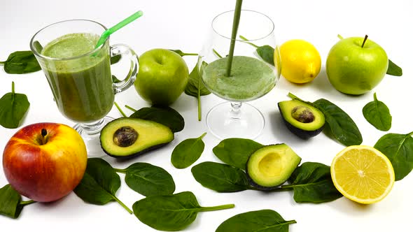 Glass mug with a smoothie, lemon, fresh spinach leaves, avocado and apples are on a table