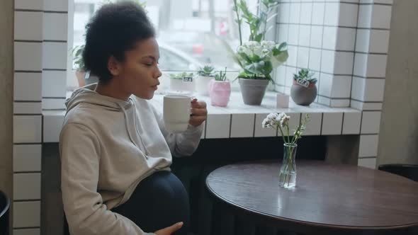 Pregnant Young African American Woman Drinks Herbal Tea at the Cafe
