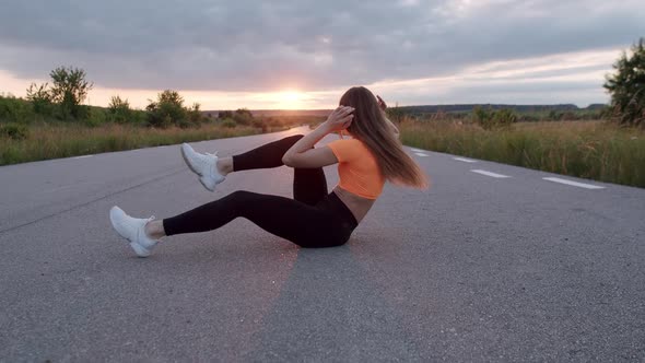 Young Athletic Girl Doing Abs Exercises Flexing Legs on Road at Nature alt