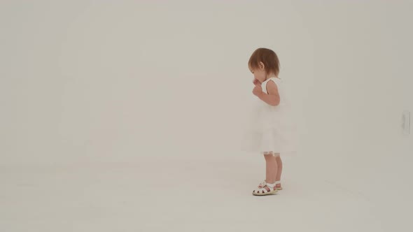 Little Girl in Dress is Playing on the White Carpet alt
