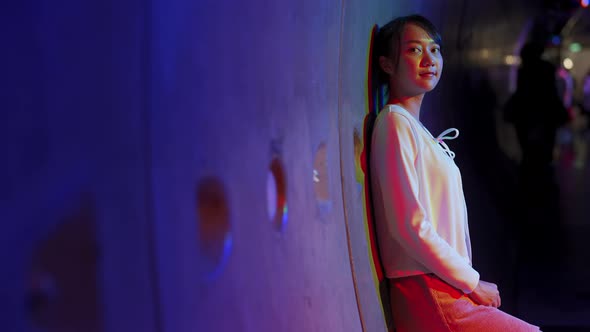 4K Portrait of Young Asian woman walking down city street with illuminated neon lights at night.