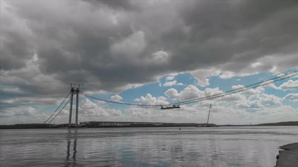 Suspended bridge, under construction over big river, right before a storm. alt