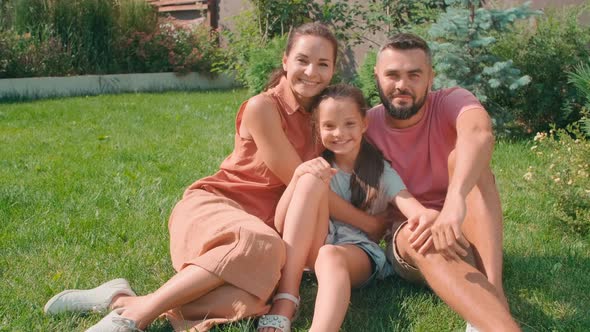 Happy Family Of Three Sitting On Lawn In Summer alt