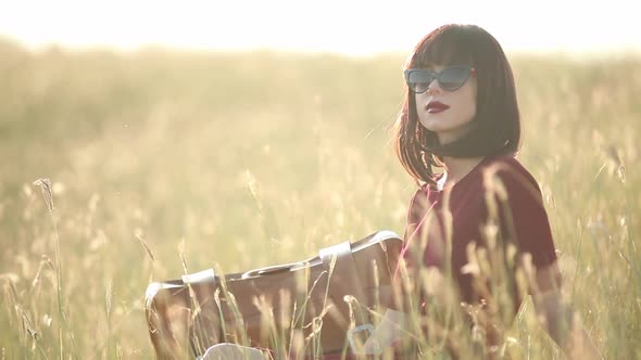 Brunette girl with sunglasses sitting on grass.