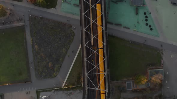 Yellow Subway Train on Bridge Passing Public Park in Berlin, Germany, Aerial Birds Eye Overhead Top alt