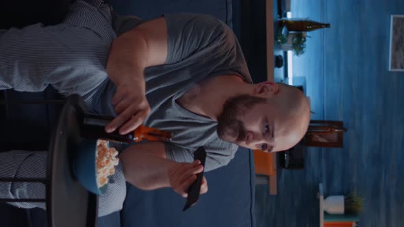 Vertical Video Bored Man Changing Tv Channels Sitting on Cozy Couch Drinking Beer alt
