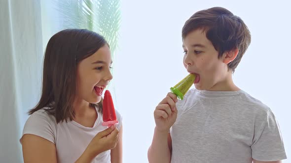 A Cute Girl and a Boy are Eating Colorful Homemade Ice Cream While Standing at Home