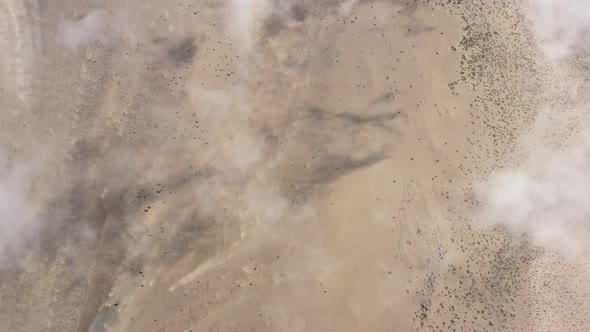 Flying above white thin clouds leaving a shadow behind on the land with brown sand and rocks alt