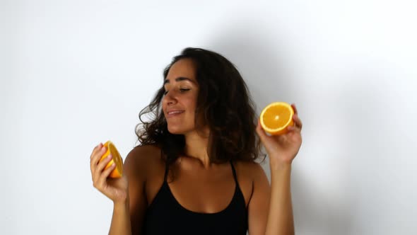 A beautiful mixed-race woman with dark hair smiling and dancing with oranges. alt