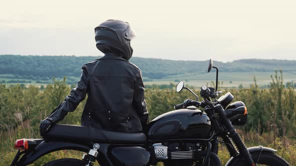 Stylish Motorcyclist Woman in Helmet and Leather Jacket Sitting on Vintage Motorcycle alt