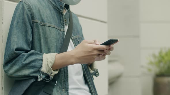 Young Asian man wearing a surgical mask and using smartphone.