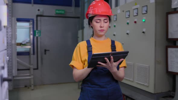 A young female engineer walks through the production room and writes data into a tablet. alt