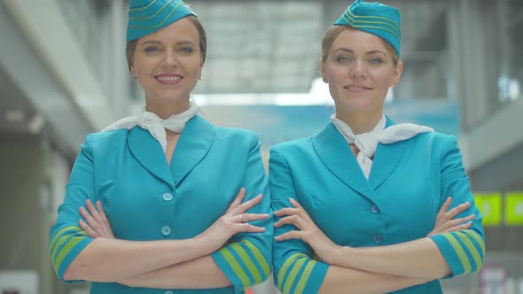 Portrait of Two Beautiful Caucasian Women in Stewardess Uniform with Hands Crossed Looking at Camera alt