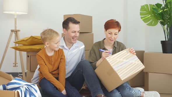 Young Caucasian Family Writing on Cardboard Boxes for Moving Day