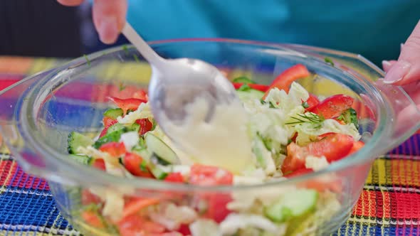 Caucasian Woman Adding White Sauce in Glass Bowl with Vegetable Salad and Mixing It with Steel Spoon