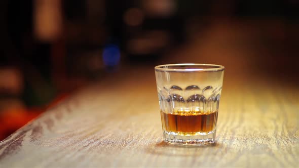 Glass of whiskey with a person adding ice cubes, in a pub