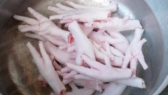 Close up Inox pan with uncooked Chicken feet on water, hand adding Chicken feet piece alt
